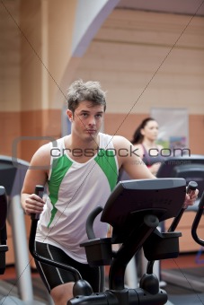 Handsome man doing exercises using cross trainer in a fitness ce