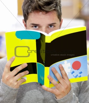 Male student standing in a book shop hiding his face behind a bo