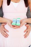 Close-up of the belly of a pregnant woman holding baby shoes and