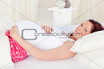 Caucasian pregnant woman resting n her bed in the bedroom