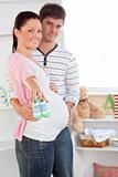 Cheerful pregnant woman holding baby shoes while husband touchin