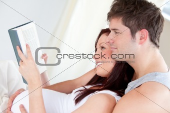 Close-up of a pregnant woman and her husband reading a book on t
