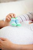 Close-up of the belly of a pregnant woman holding baby shoes and