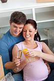 Joyful couple expecting a baby drinking and sitting on the floor