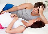 cute man touching the belly of his pregnant wife lying on the be