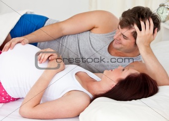 cute man touching the belly of his pregnant wife lying on the be