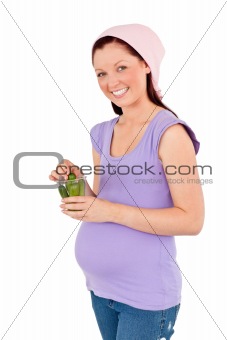 cute future mom holding gherkins in a glass smiling at the camera