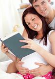 cheerful future parents reading a book sitting on their bed duri