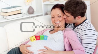 young man kissing his pregnant wife with baby letters on the belly
