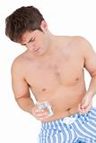 bare-chested man in pyjamas holding pills and a glass of water