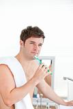thoughtful man brushing his tooth with towel on his shoulder