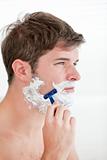 portrait of a serious man shaving looking away standing in the b