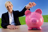 Woman Putting Coin Into Pink Piggy Bank In Green Field