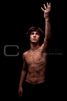 young man in topless looking up to the light and raising arm - sign of faith , isolated on black, studio shot