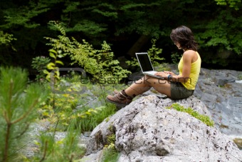 Girl with a laptop, sitting on a rock
