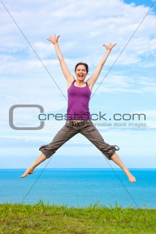 Beautiful young woman jumping and laughing by the ocean