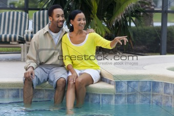 Happy African American Couple Sitting By Swimming Pool Pointing