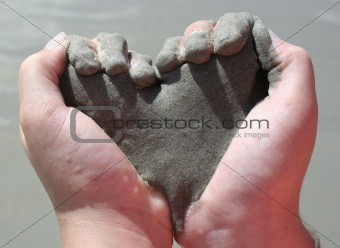 child’s hands holding sand shaped like heart