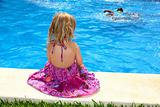 Little blond girl sitting rear back swimming pool