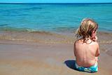 Little blond girl sit in beach shore looking ocean