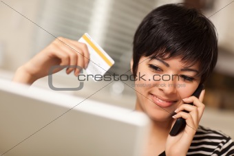 Pretty Young Multiethnic Woman Holding Phone and Credit Card Using Laptop.