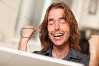 Young Man Using A Laptop Computer and Cheering with Fists in the Air.