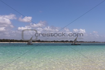 Sailing boats in ocean near white sand beach with blue sky