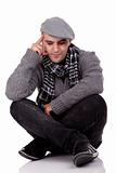 Portrait of a young man sitting on the floor, thinking and looking down, in autumn/winter clothes, isolated on white, Studio shot