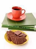 Chocolate cookie and cup of coffee on magazines isolated on whit