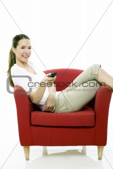 Young woman sitting on a chair with remote control on white background studio