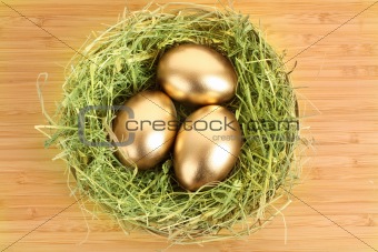 Three golden hen's eggs in the grassy nest on the wooden table