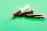 Medical test tubes and syringe with blood on green