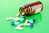 Pill bottle with white and blue pills on green