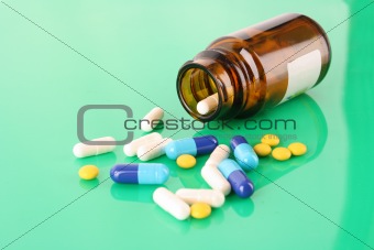 Pill bottle with coloured pills on green