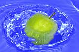 Green apple with water splash on blue water background
