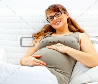 Smiling beautiful pregnant woman lying on couch and holding her belly.
