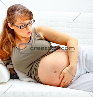 Beautiful pregnant woman lying on sofa and blowing kiss her belly.

