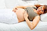 Smiling beautiful pregnant woman relaxing on sofa and  holding her tummy.
