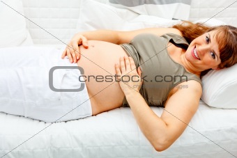 Smiling beautiful pregnant woman relaxing on sofa and  holding her tummy.
