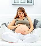 Beautiful pregnant woman sitting on sofa and blowing kiss her belly.
