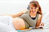 Smiling beautiful pregnant woman relaxing on sofa with magazine.
