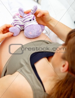 Pregnant woman sitting on sofa and holding toy on her belly.
