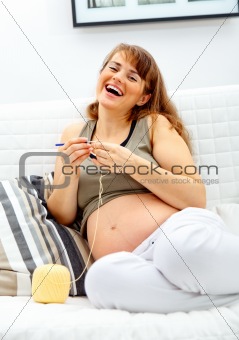 Laughing beautiful  pregnant woman knitting  for her baby.
