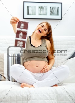 Laughing beautiful pregnant  female sitting on sofa with echo in hand.
