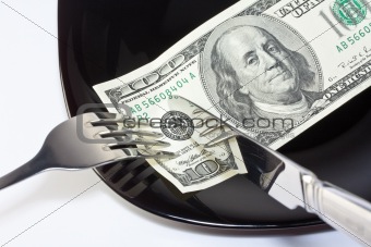 Banknote on a black plate with knife and fork