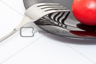 Red tomato on a black plate with fork