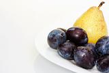 Yellow pear on a white plate with plums