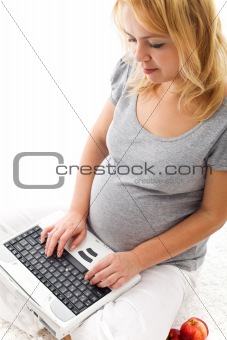 Beautiful pregnant woman sitting on the floor with laptop