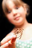girl holding brown spider by one leg and looking surprised