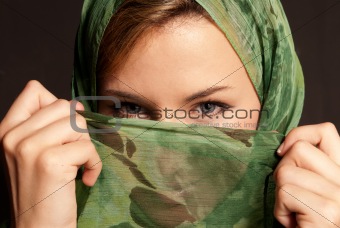 Young Arab woman with veil showing her eyes on dark gray background